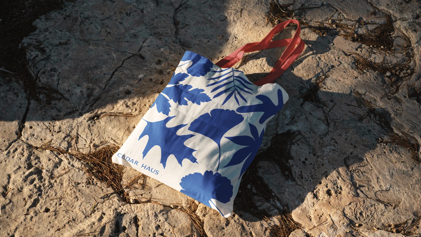Branded tote bag with botanical leaf pattern on rocky beach